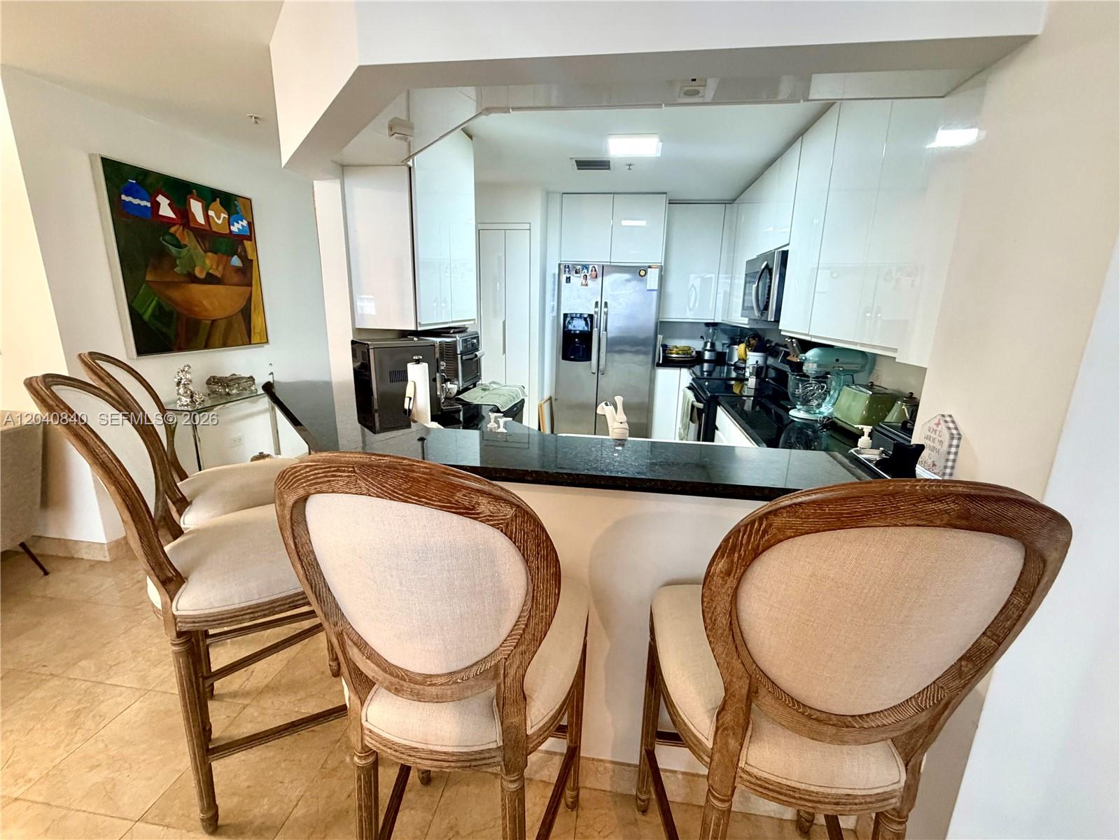 A kitchen features white cabinets, black countertops, and three upholstered bar stools at a counter — 801 Brickell Key Blvd # 1704, Miami FL 33131, MIAMI, FL