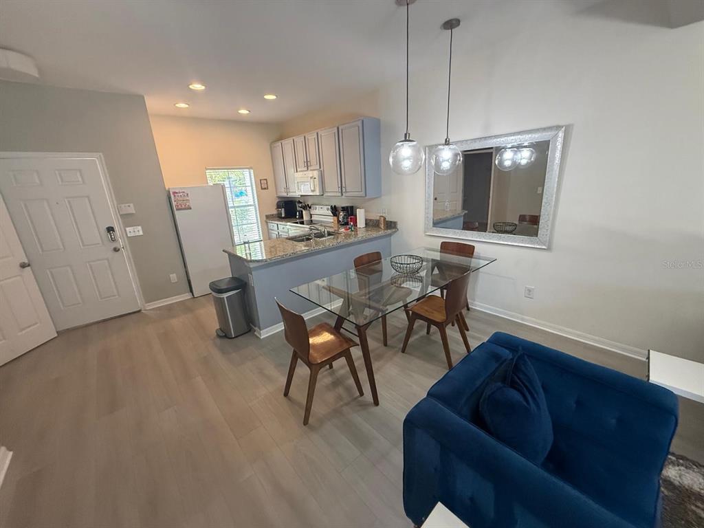 An open-concept kitchen and dining area features light wood flooring, gray cabinets, and glass furniture — 4564 ADA LANE, KISSIMMEE, FL