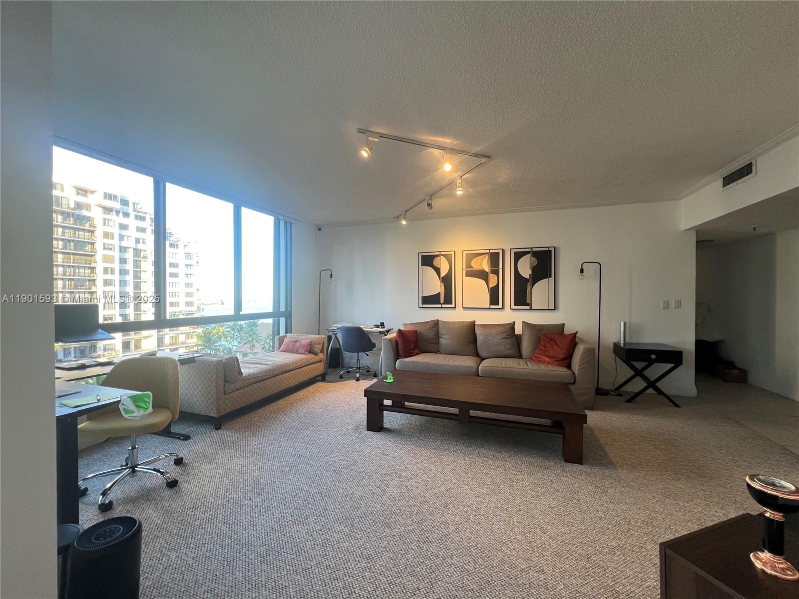 A living room features a sofa, coffee table, desk, and large windows with city views — 520 Brickell Key Dr # A900, Miami FL 33131, MIAMI, FL
