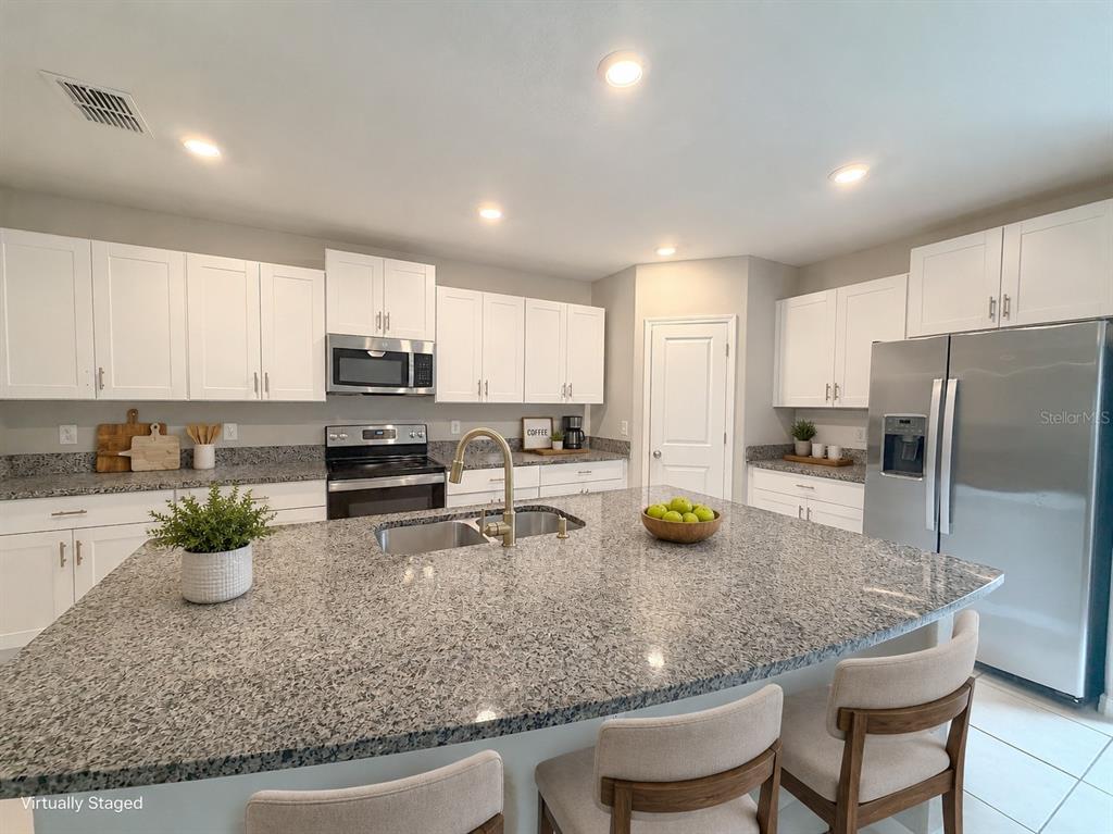 A kitchen features white cabinets, granite countertops, a large island, and stainless steel appliances — 2122 STELLAR BRILLIANCE WAY, LUTZ, FL
