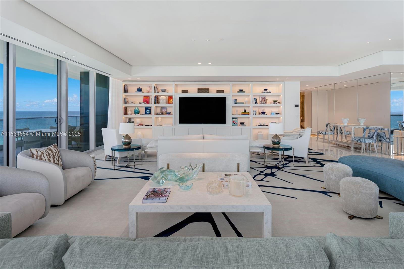 A modern living room features white built-in shelving, a large television, and ocean views — 9349 Collins Ave # 1101, Surfside FL 33154, SURFSIDE, FL