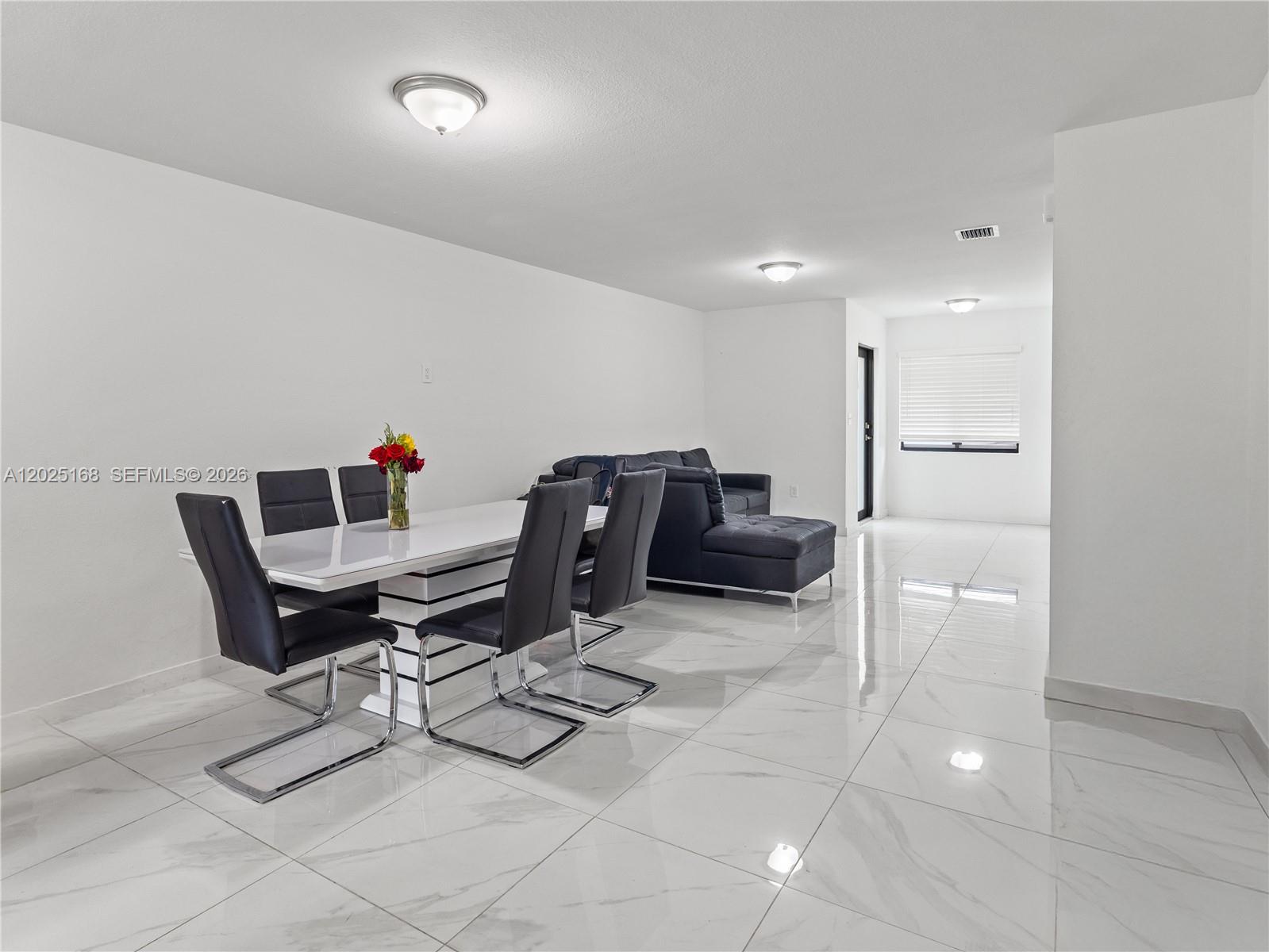 A dining area with a white table and black chairs sits next to a living room — 10769 SW 146th St, Miami FL 33176, MIAMI, FL