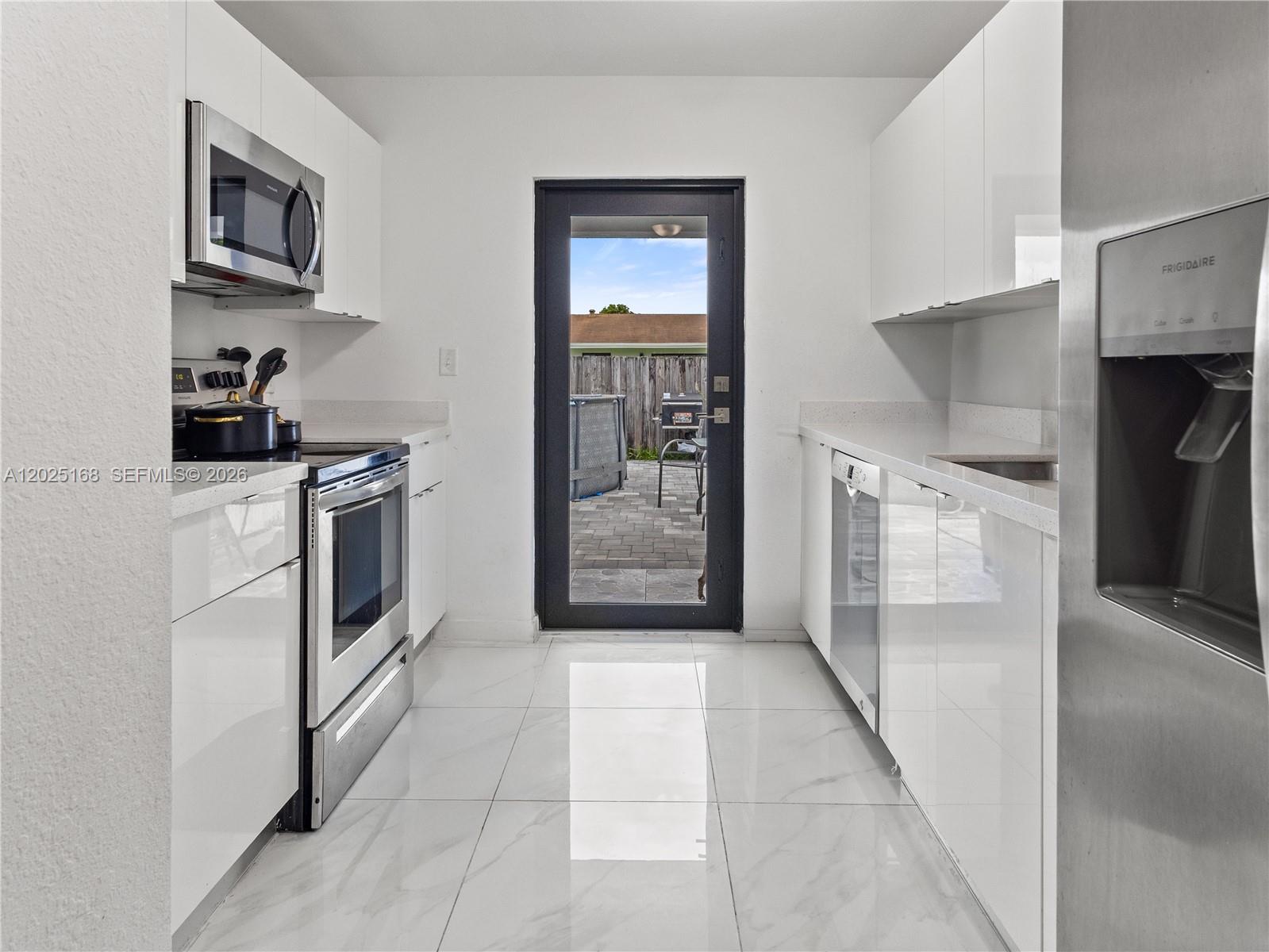 A galley kitchen features white glossy cabinets, stainless steel appliances, and a glass-paned exterior door — 10769 SW 146th St, Miami FL 33176, MIAMI, FL