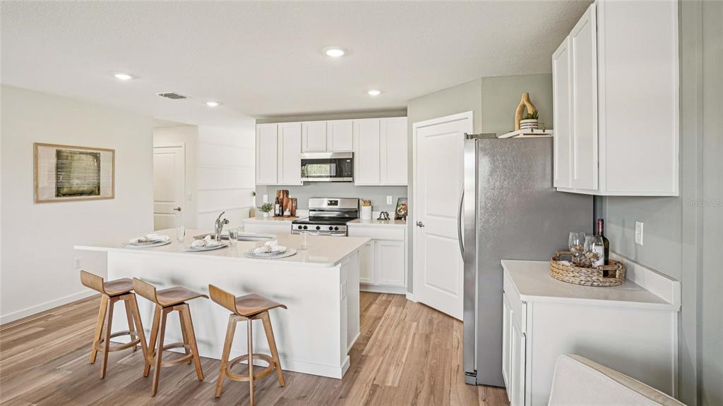 A modern kitchen features white cabinetry, a central island with bar stools, and stainless appliances — 15952 SE 101ST CIRCLE, SUMMERFIELD, FL