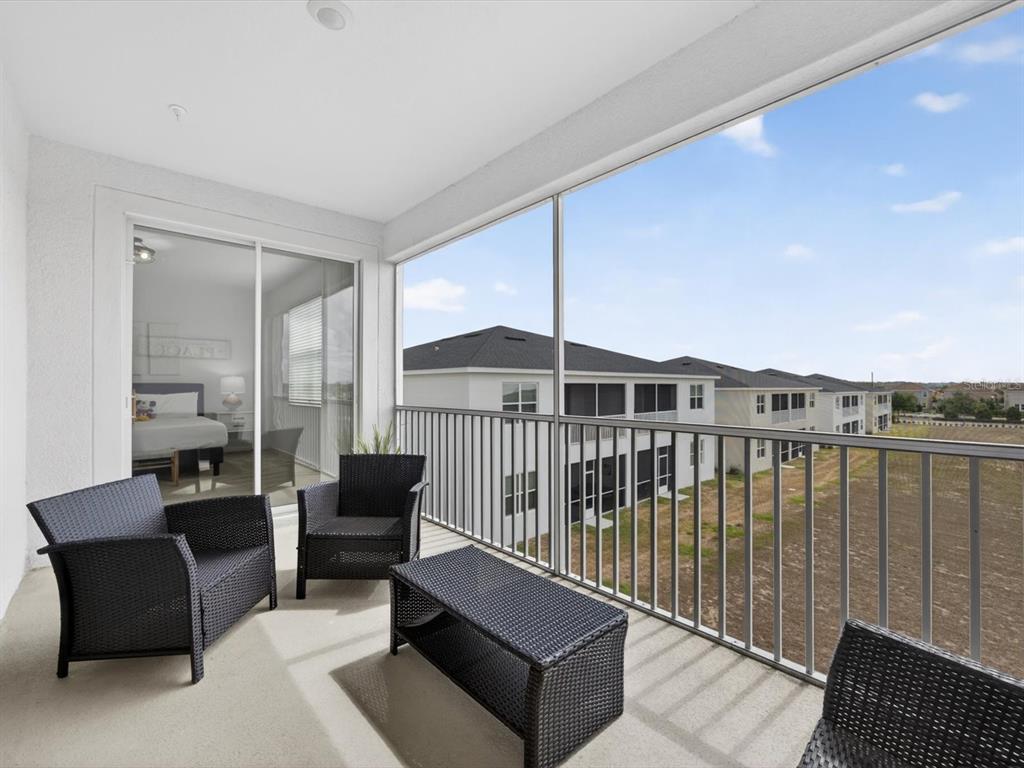A covered balcony features dark wicker furniture and a metal railing overlooking a grassy field — 967 SPLASH SHOT PLACE UNIT 2503, DAVENPORT, FL