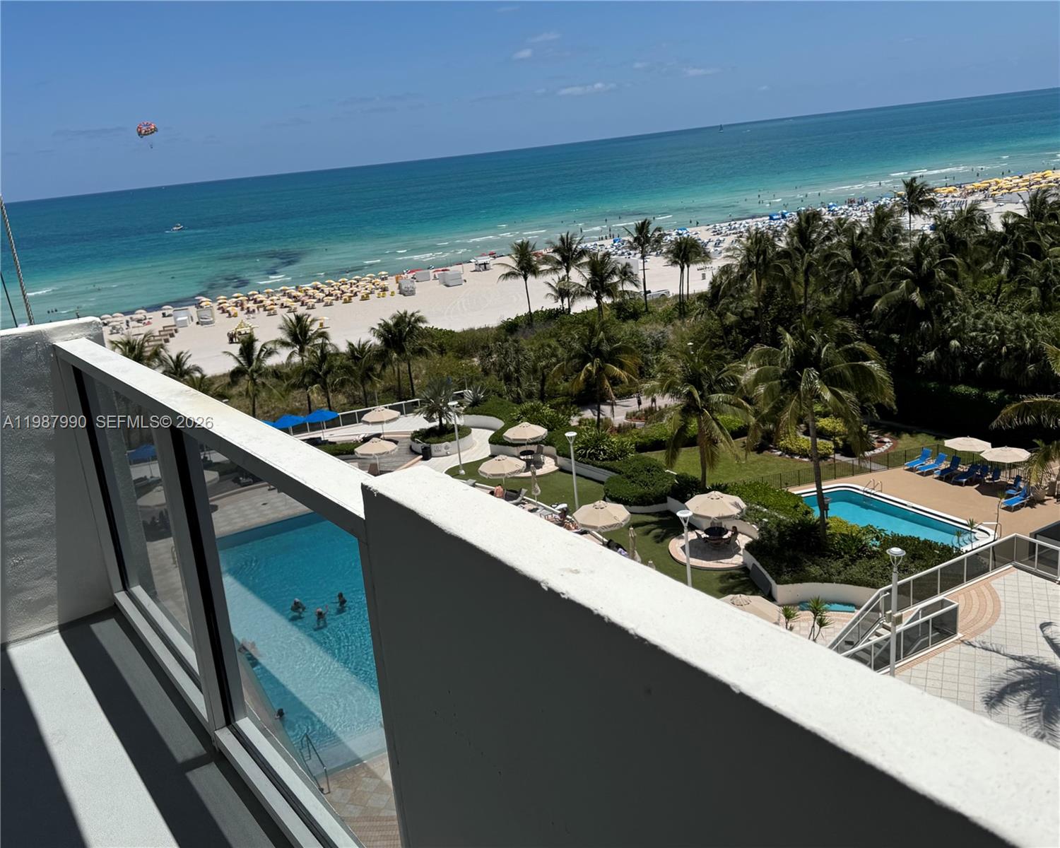 A high-angle view from a balcony overlooks a swimming pool, palm trees, and the beach — 100 Lincoln Rd # 836, Miami Beach FL 33139, MIAMI BEACH, FL