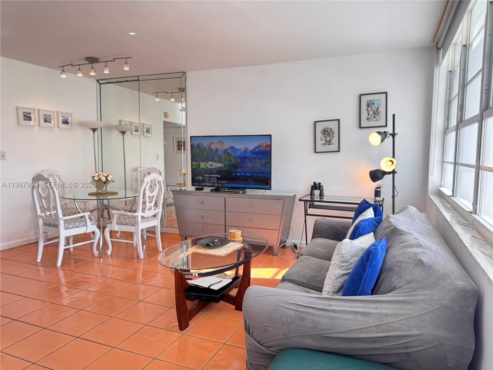 A living and dining area features orange tile flooring, a grey sofa, and mirrored walls — 100 Lincoln Rd # 836, Miami Beach FL 33139, MIAMI BEACH, FL