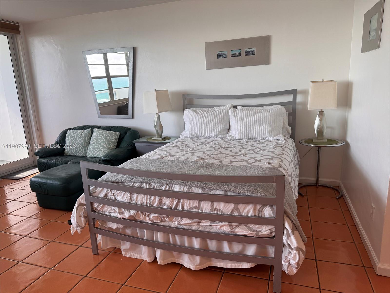 A bedroom features a metal bed frame, a green leather chair, and terracotta tile flooring — 100 Lincoln Rd # 836, Miami Beach FL 33139, MIAMI BEACH, FL