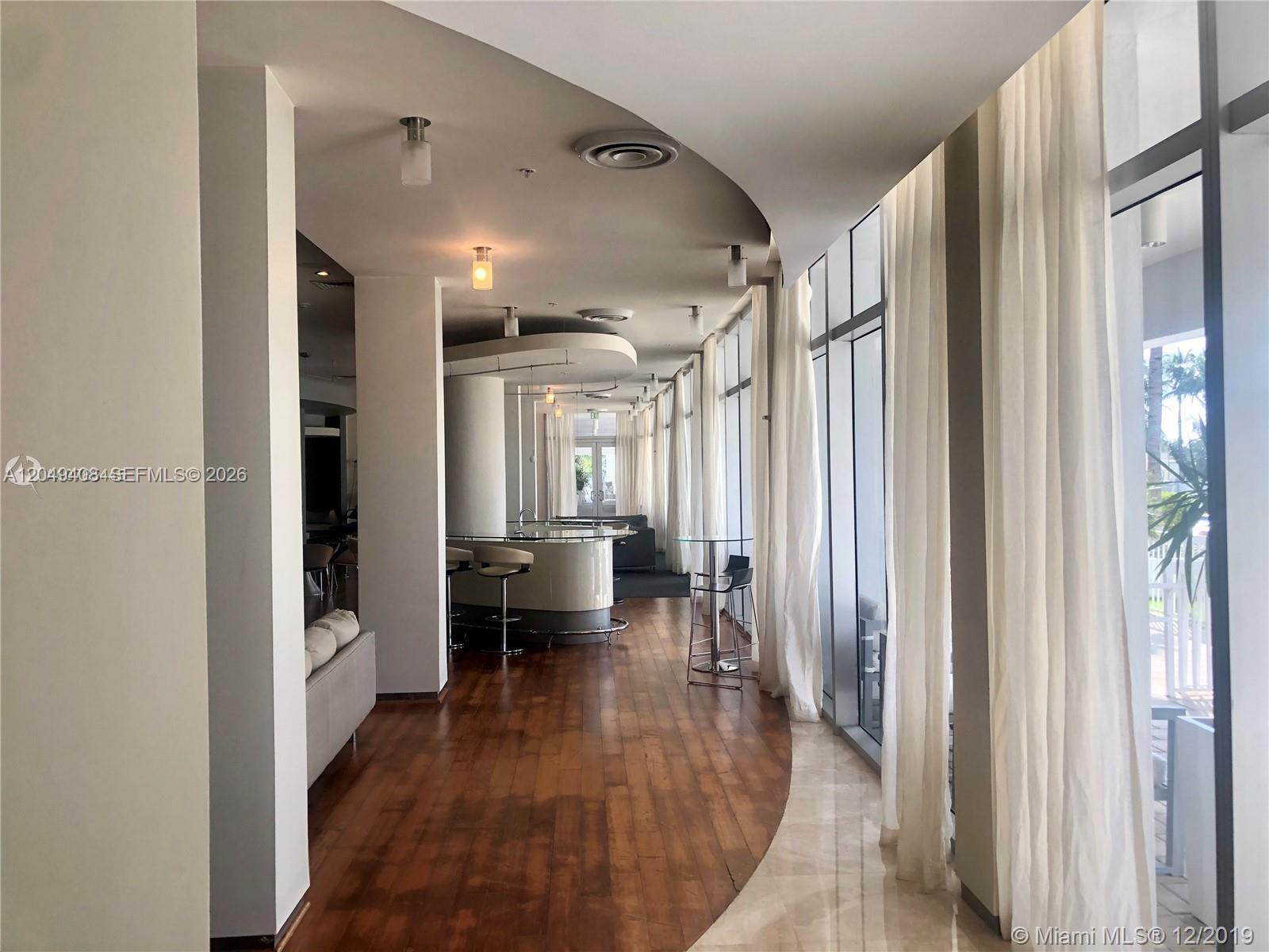 A modern lounge area features a curved bar, wood flooring, and floor-to-ceiling windows with curtains — 10275 Collins Ave # 230, Bal Harbour FL 33154, BAL HARBOUR, FL