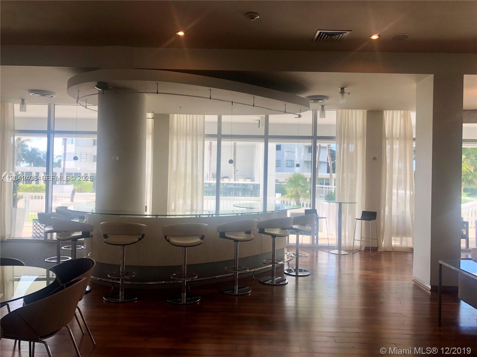 A curved bar with stools sits in a room with floor-to-ceiling windows and wood flooring — 10275 Collins Ave # 230, Bal Harbour FL 33154, BAL HARBOUR, FL