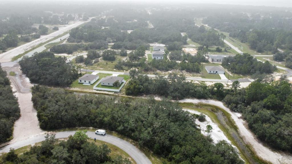 An aerial view shows several houses situated among wooded lots and unpaved roads — 1255 BALTIC DRIVE, POINCIANA, FL