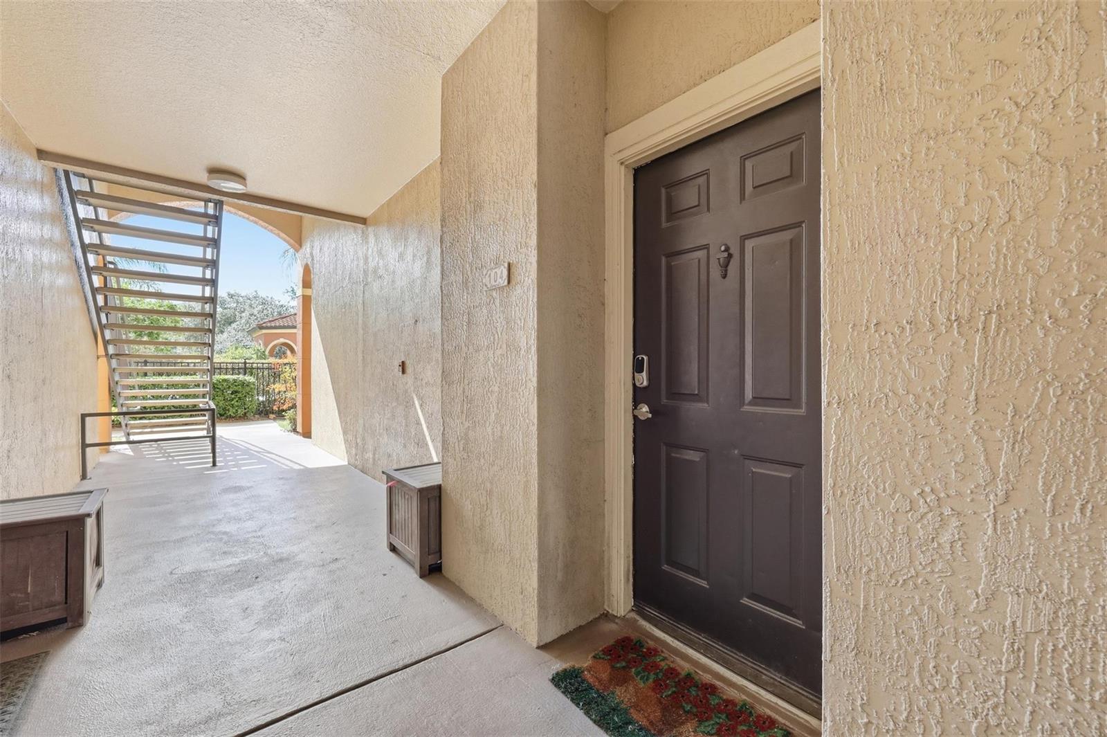 A dark brown front door with a digital lock sits on a covered concrete patio — 5518 Metrowest Boulevard # 104, Orlando FL 32811, ORLANDO, FL