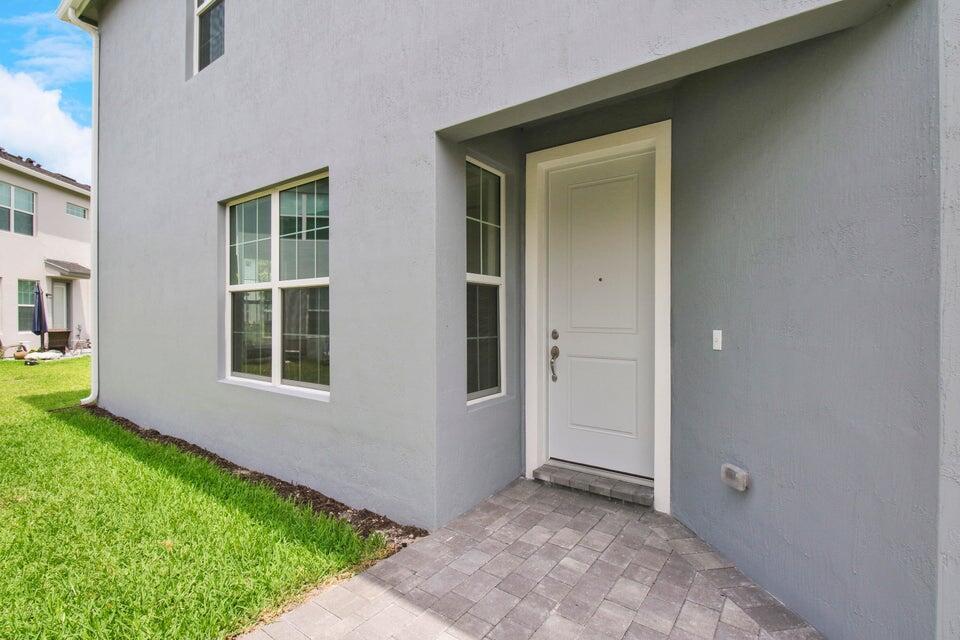 A gray stucco exterior features a white front door, a side window, and paver walkway — 1875 SE Ocean Cove Way, Stuart FL 34996, STUART, FL