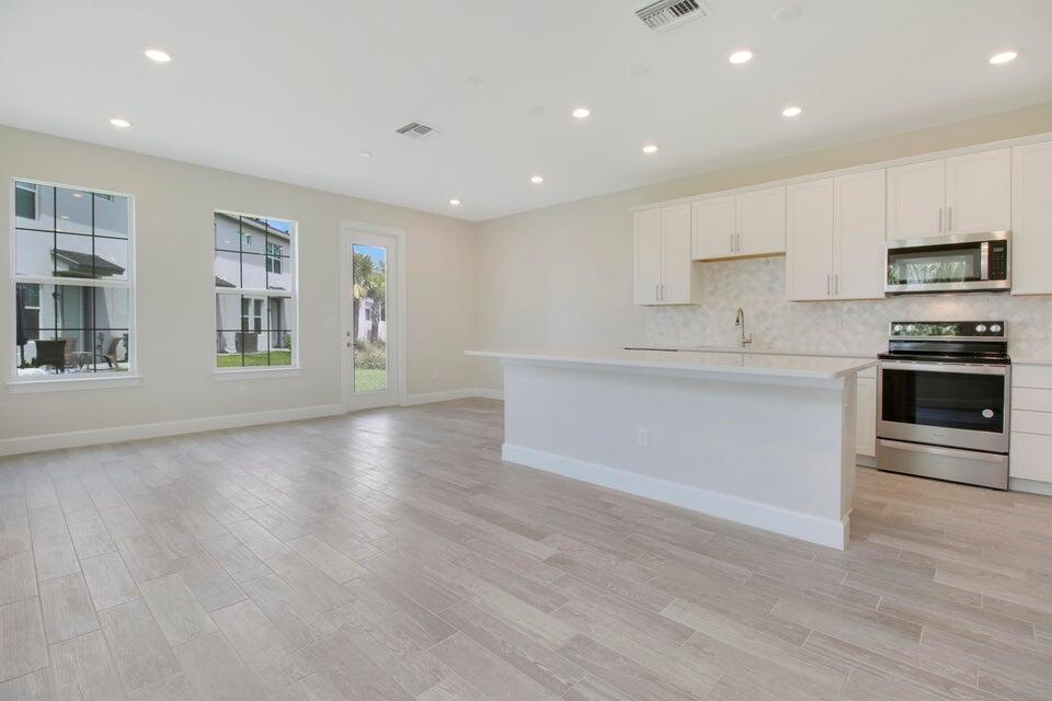 A modern kitchen features white cabinets, stainless steel appliances, and light wood-look tile flooring — 1875 SE Ocean Cove Way, Stuart FL 34996, STUART, FL