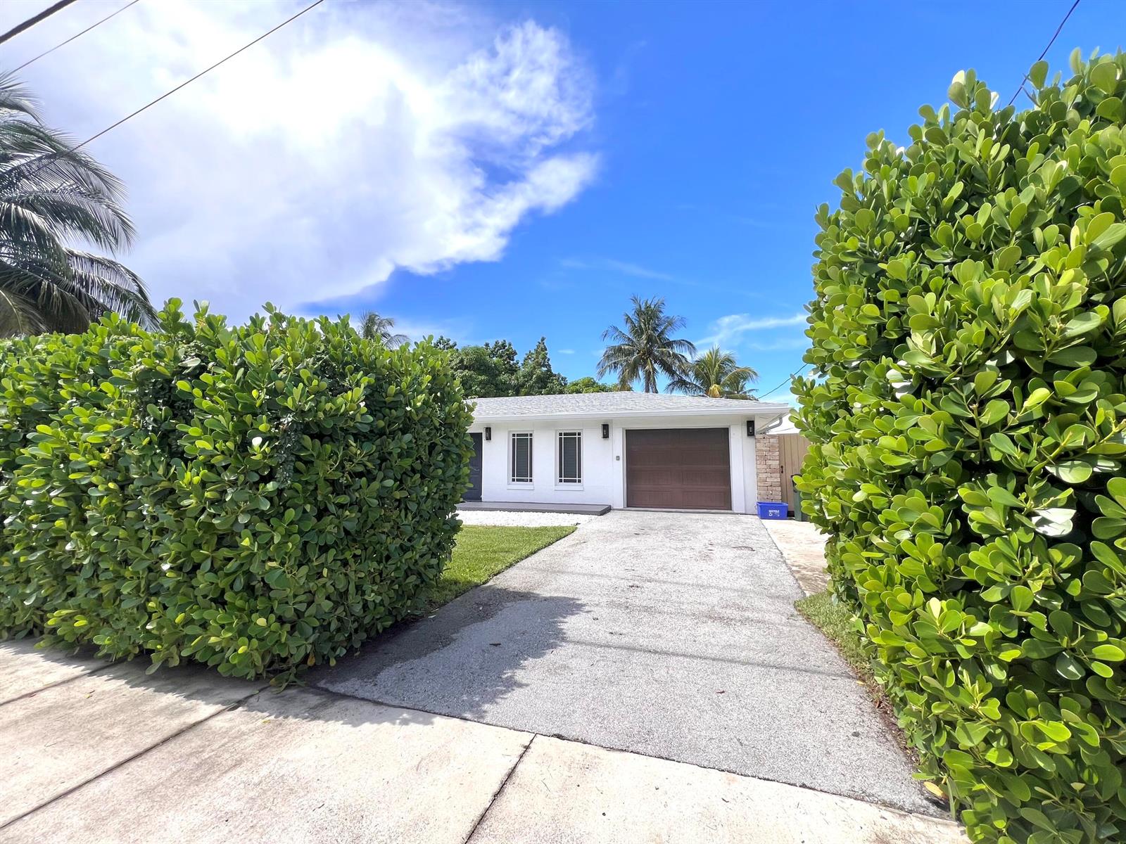 A white house with a brown garage door sits behind a driveway and large hedges — 902 S Swinton Avenue, Delray Beach FL 33444, DELRAY BEACH, FL