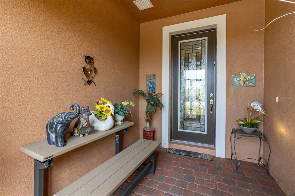 A covered entryway features a brick floor, a brown front door, and a decorative bench — 677 VIA CORSO COURT, KISSIMMEE, FL