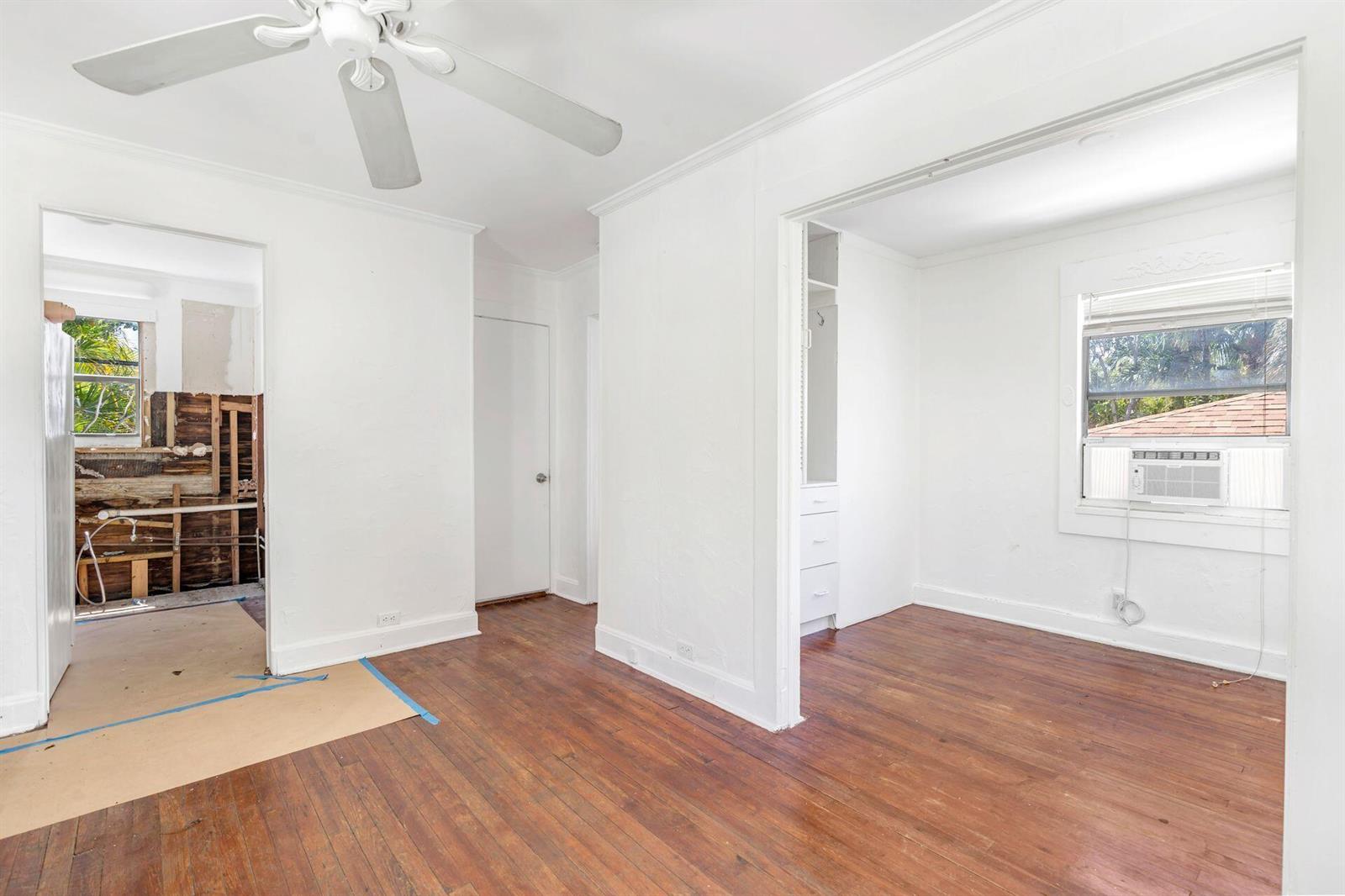 An interior view shows a room with hardwood floors, a ceiling fan, and an adjacent renovation — 214 Conniston Road, West Palm Beach FL 33405, WEST PALM BEACH, FL