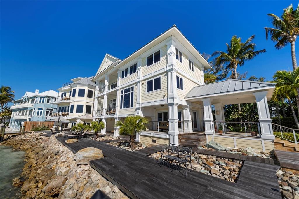A multi-story yellow house with a wooden deck sits along a rocky shoreline — 3750 BAYOU LOUISE LANE, SARASOTA, FL
