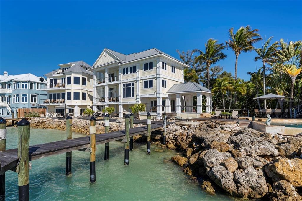 A multi-story yellow house with a wooden dock extending into the water — 3750 BAYOU LOUISE LANE, SARASOTA, FL