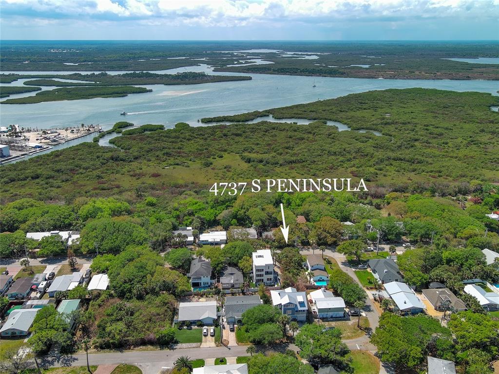 An aerial view shows a multi-story house nestled among trees near a coastal waterway — 4737 S. PENINSULA DRIVE, PONCE INLET, FL