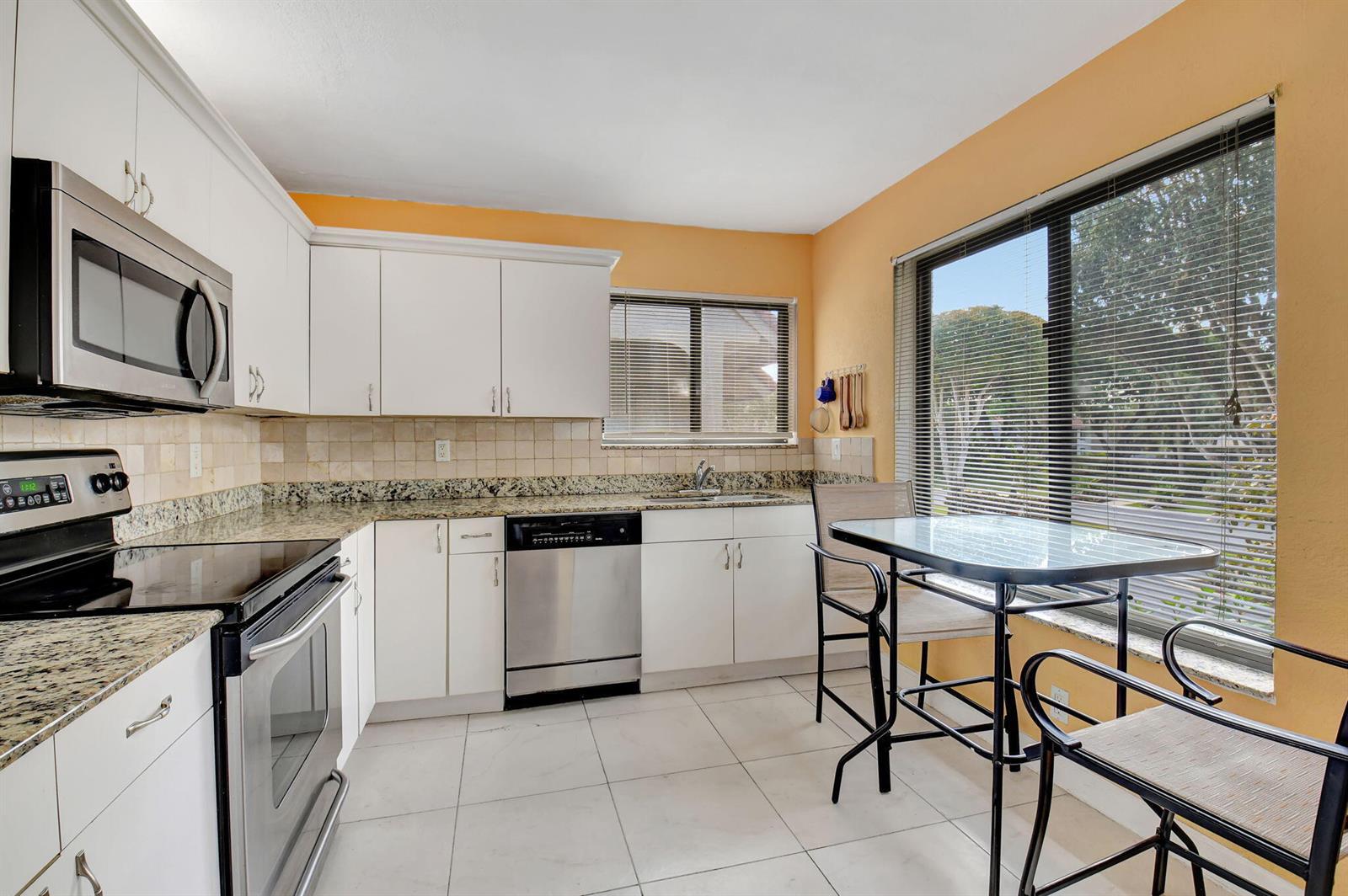 A kitchen with white cabinets, granite countertops, stainless steel appliances, and a small dining table — 5715 Fairway Park Drive # 201, Boynton Beach FL 33437, BOYNTON BEACH, FL
