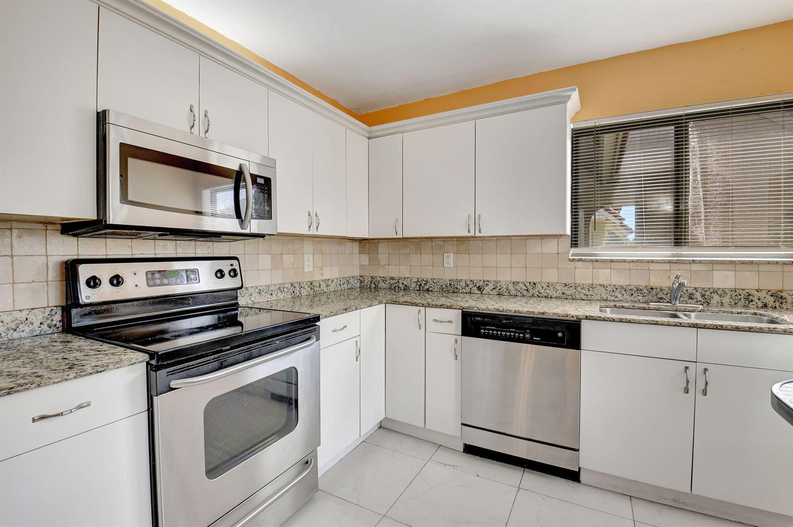 A kitchen features white cabinets, granite countertops, stainless steel appliances, and a tiled backsplash — 5715 Fairway Park Drive # 201, Boynton Beach FL 33437, BOYNTON BEACH, FL
