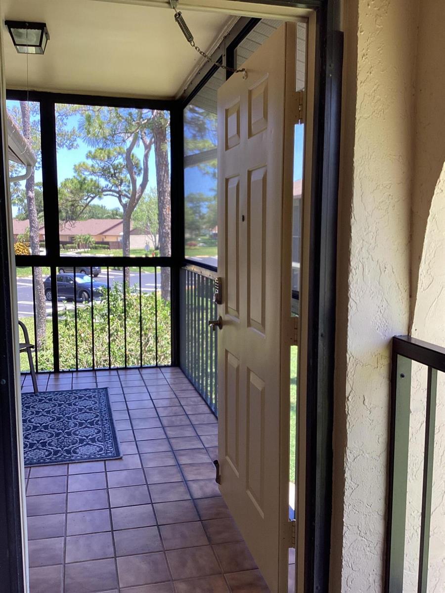 A view from a doorway looking out onto a tiled, screened-in balcony with metal railings — 410 Pine Glen Lane # 2, FL 33463, FL