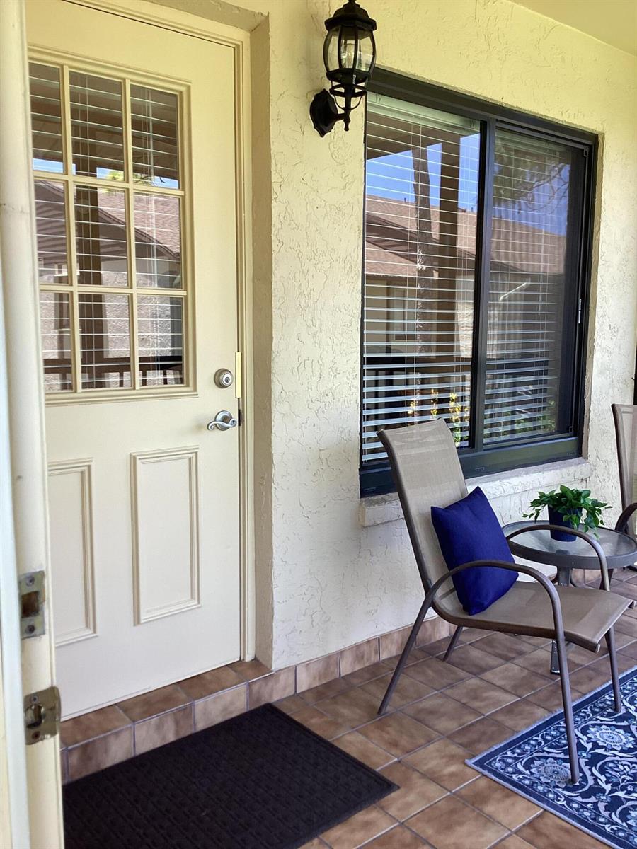 A covered patio features a beige door, a window with blinds, and outdoor seating — 410 Pine Glen Lane # 2, FL 33463, FL