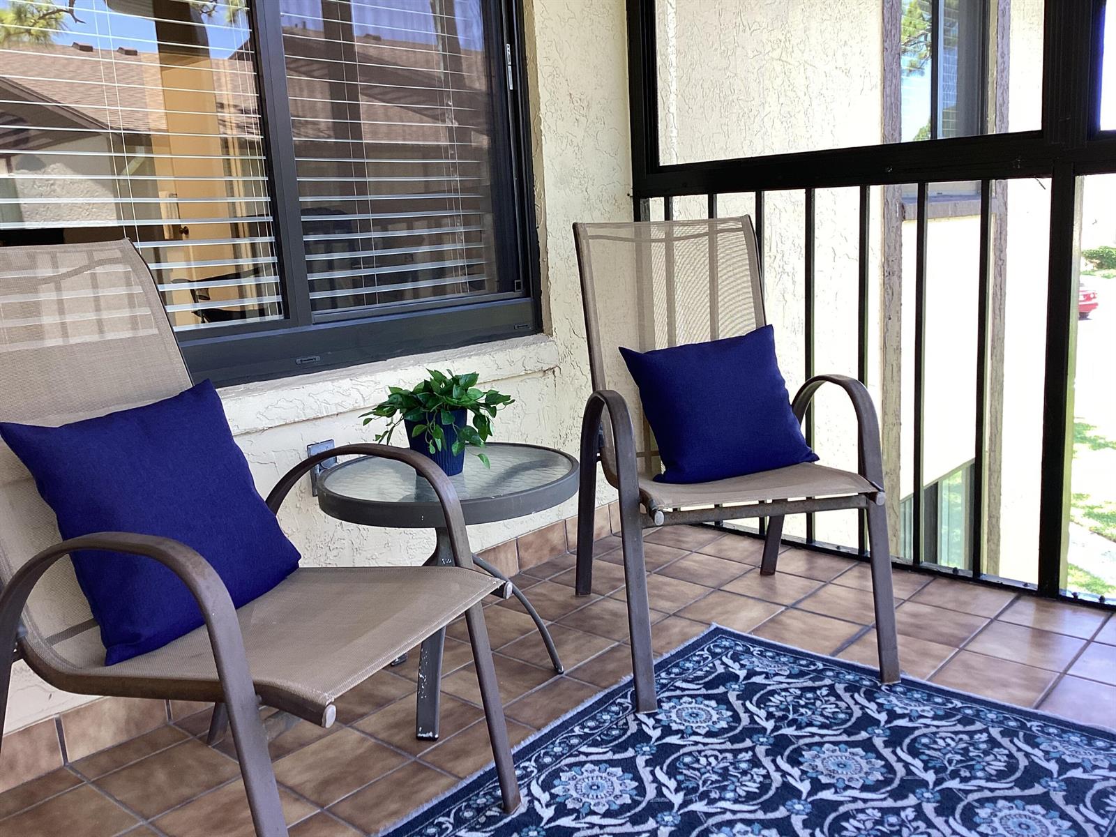 A covered patio features two chairs with blue pillows, a small glass table, and tile flooring — 410 Pine Glen Lane # 2, FL 33463, FL