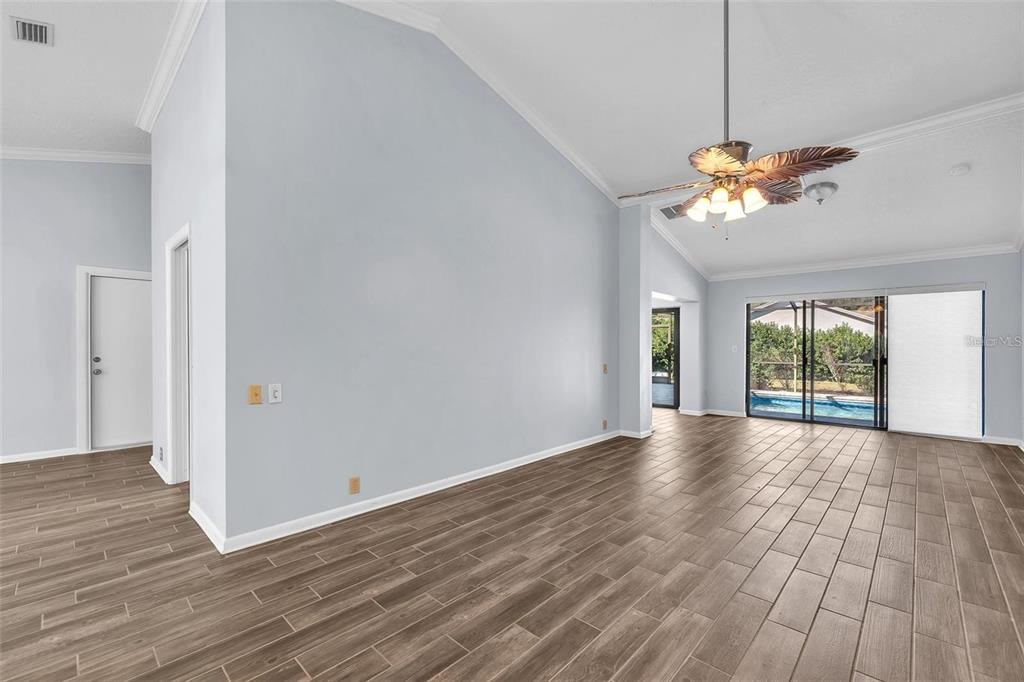 An empty living room features vaulted ceilings, wood-look tile flooring, and sliding glass doors — 1702 HORSESHOE DRIVE, PLANT CITY, FL