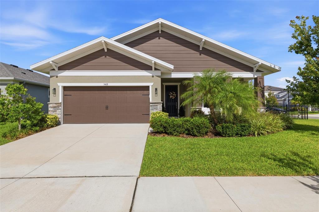 A single-story suburban house with a brown garage, tan siding, and a landscaped front yard — 5408 TAGALONG PLACE, APOLLO BEACH, FL