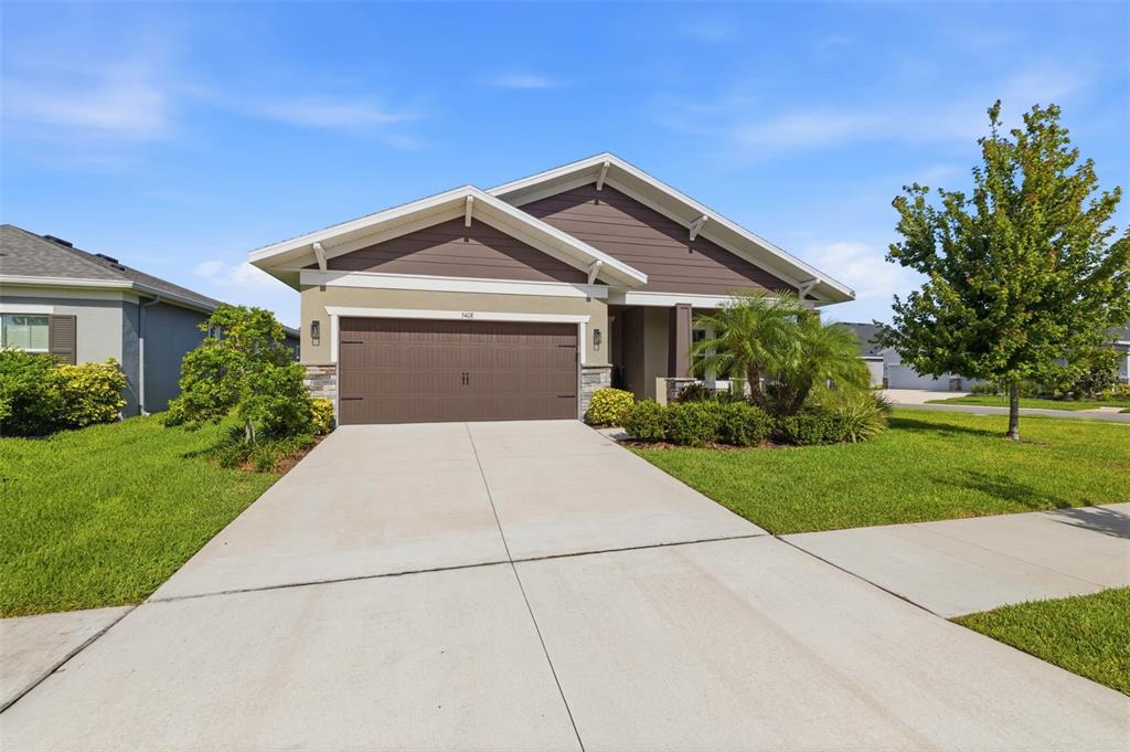 A single-story house with a brown garage door, tan stucco walls, and a concrete driveway — 5408 TAGALONG PLACE, APOLLO BEACH, FL