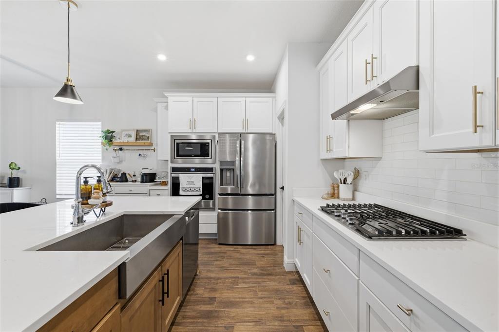 A modern kitchen features white cabinetry, stainless steel appliances, a farmhouse sink, and wood flooring — 5408 TAGALONG PLACE, APOLLO BEACH, FL