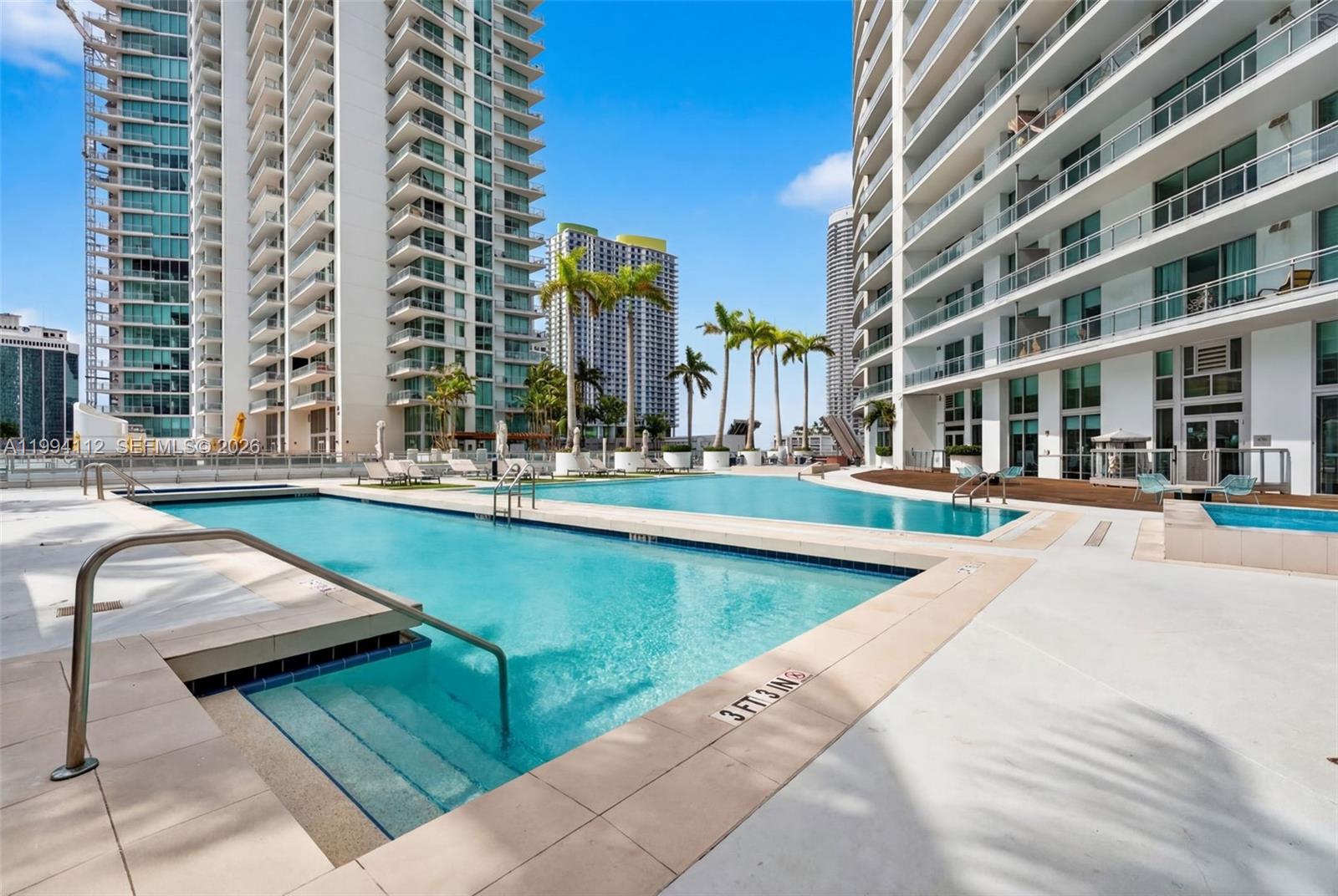 A large outdoor swimming pool is situated between two tall modern residential high-rise buildings — 90 SW 3rd St # 1105, Miami FL 33130, MIAMI, FL