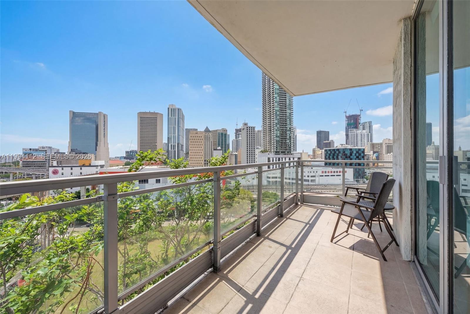 A balcony with two chairs overlooks a city skyline under a clear blue sky — 90 SW 3rd St # 1105, Miami FL 33130, MIAMI, FL
