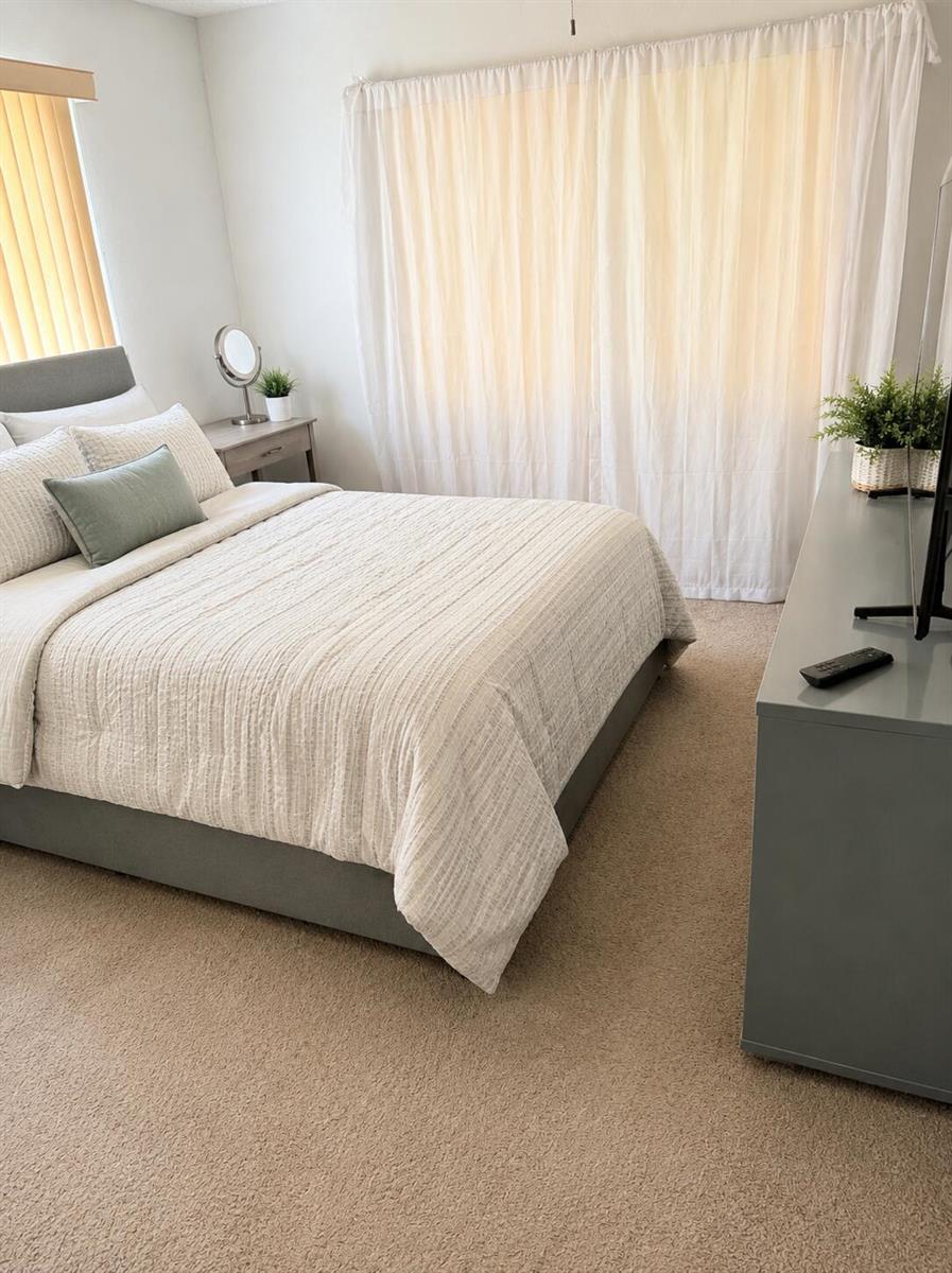 A bedroom features a gray upholstered bed, a matching dresser, and sheer white curtains — 305 Fanshaw H, Boca Raton FL 33434, BOCA RATON, FL