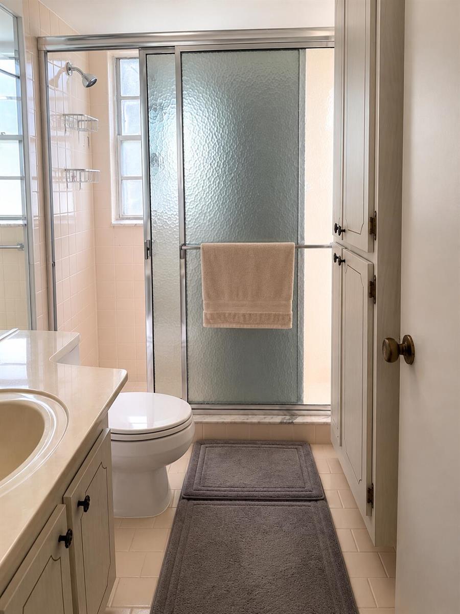 A bathroom features a vanity, a toilet, a glass-enclosed shower, and light-colored cabinetry — 305 Fanshaw H, Boca Raton FL 33434, BOCA RATON, FL