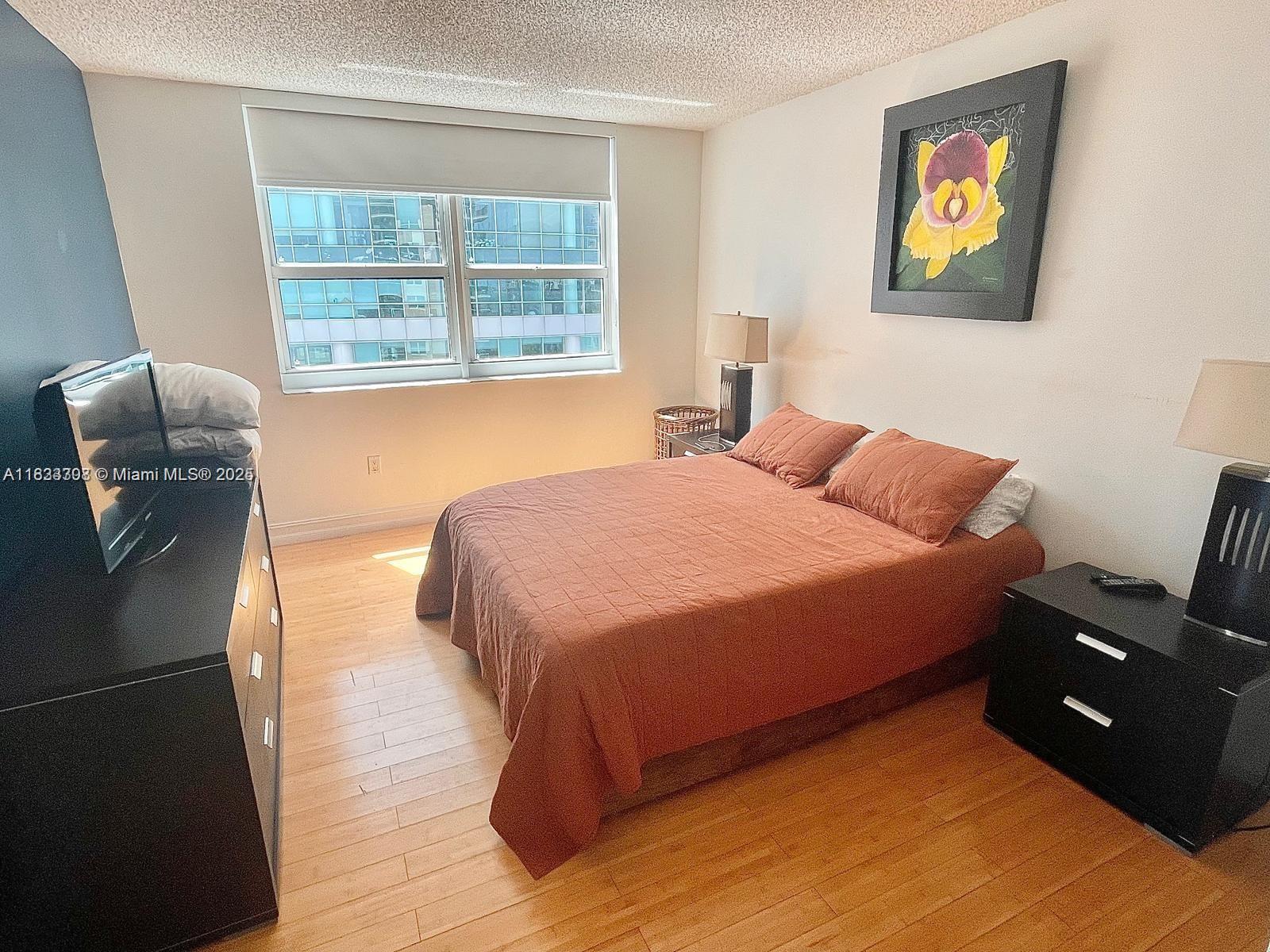 A bedroom features a bed with a rust-colored quilt, wood flooring, and a city view — 1155 Brickell Bay Dr # 1401, Miami FL 33131, MIAMI, FL