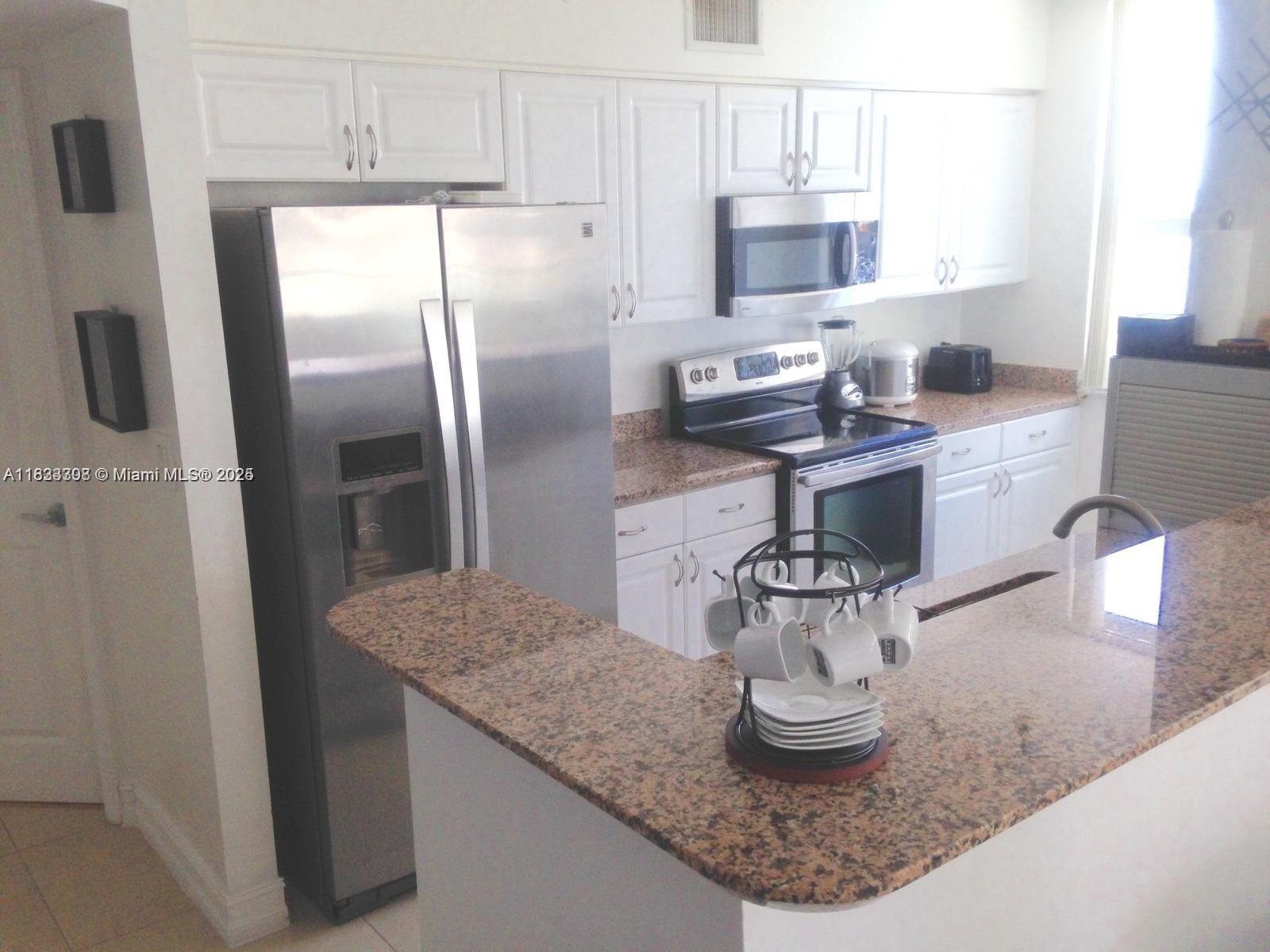 A kitchen features white cabinets, stainless steel appliances, and a granite-topped breakfast bar — 1155 Brickell Bay Dr # 1401, Miami FL 33131, MIAMI, FL