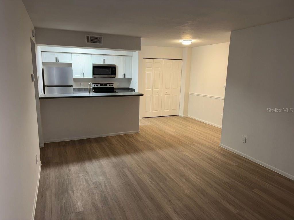 An open-concept kitchen with white cabinets and stainless steel appliances overlooks a living area — 5313 SUMMERLIN ROAD UNIT 1302, FORT MYERS, FL
