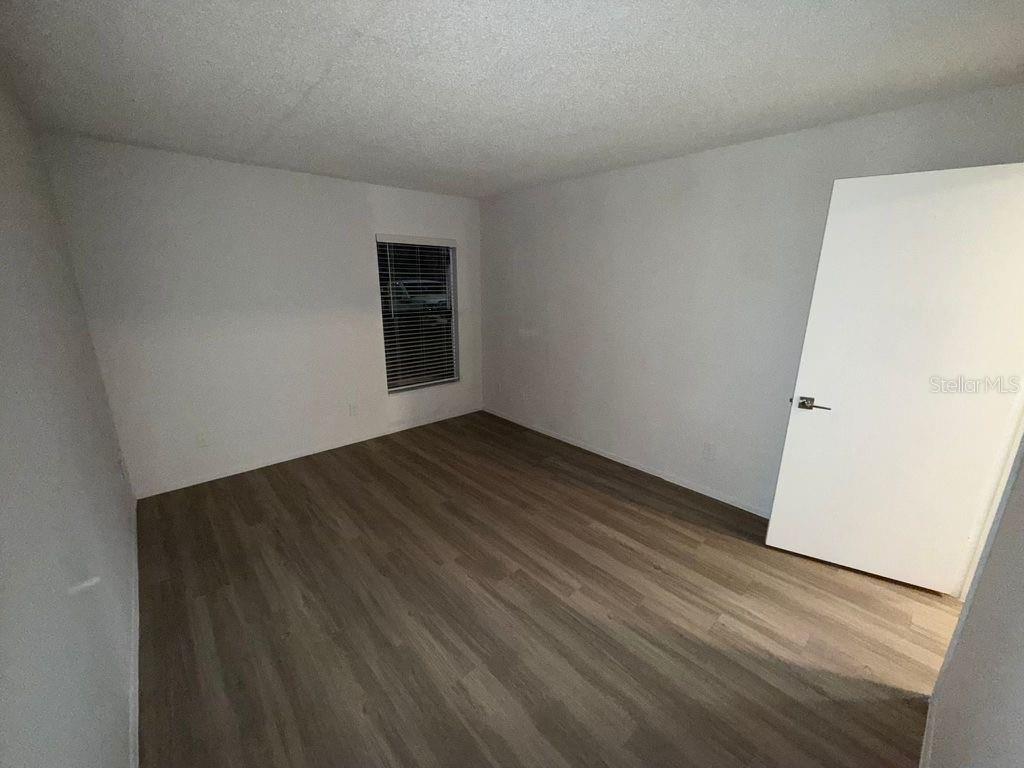 An empty bedroom features light gray walls, wood-look flooring, a single window, and a white door — 5313 SUMMERLIN ROAD UNIT 1302, FORT MYERS, FL
