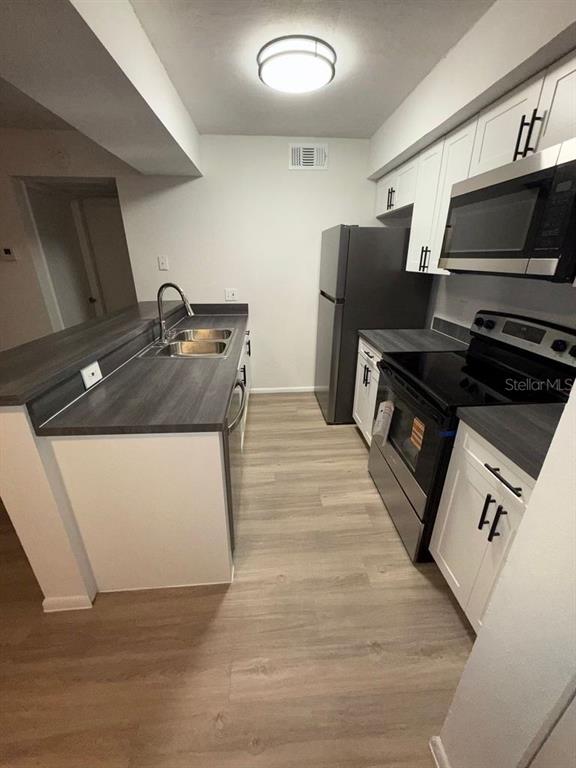 A kitchen features white cabinets, dark countertops, stainless steel appliances, and light wood-look flooring — 5313 SUMMERLIN ROAD UNIT 1302, FORT MYERS, FL