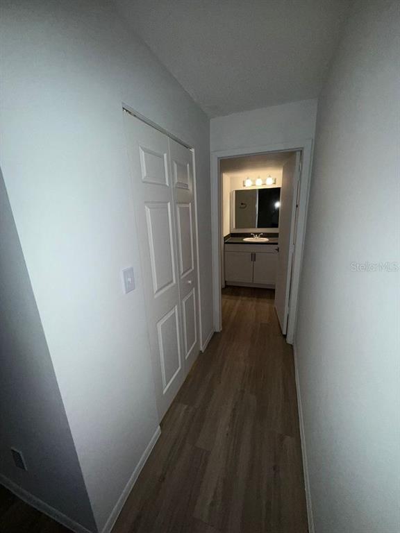 A hallway with light wood-look flooring leads to a bathroom with a vanity and mirror — 5313 SUMMERLIN ROAD UNIT 1302, FORT MYERS, FL