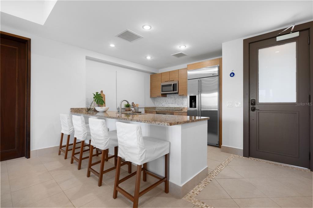 A kitchen features a granite-topped island with four white bar stools and stainless steel appliances — 7000 BAHIA BEACH BLV UNIT 8268, RIO GRANDE, PR