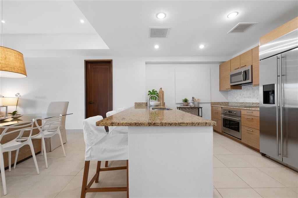 A kitchen features a granite island, light wood cabinets, stainless steel appliances, and tile flooring — 7000 BAHIA BEACH BLV UNIT 8268, RIO GRANDE, PR