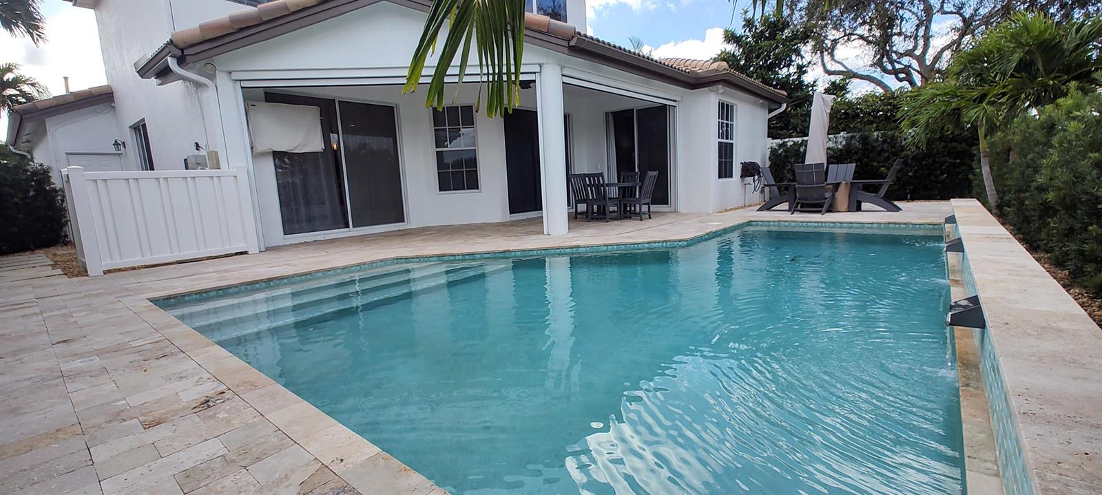 A swimming pool with stone decking sits in front of a white house with a patio — 8167 Quail Meadow Way, West Palm Beach FL 33412, WEST PALM BEACH, FL