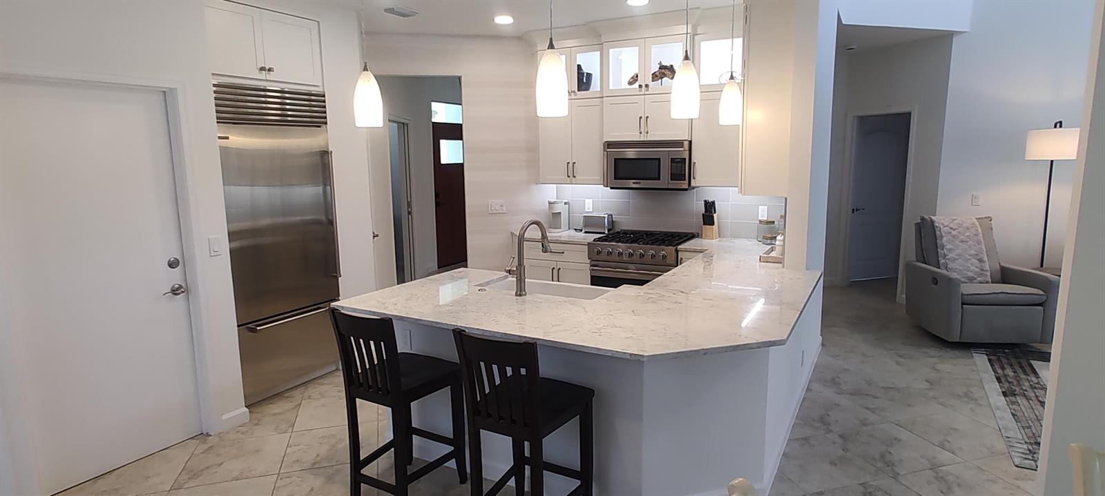 A modern kitchen features white cabinetry, stainless steel appliances, and a marble-topped island with seating — 8167 Quail Meadow Way, West Palm Beach FL 33412, WEST PALM BEACH, FL