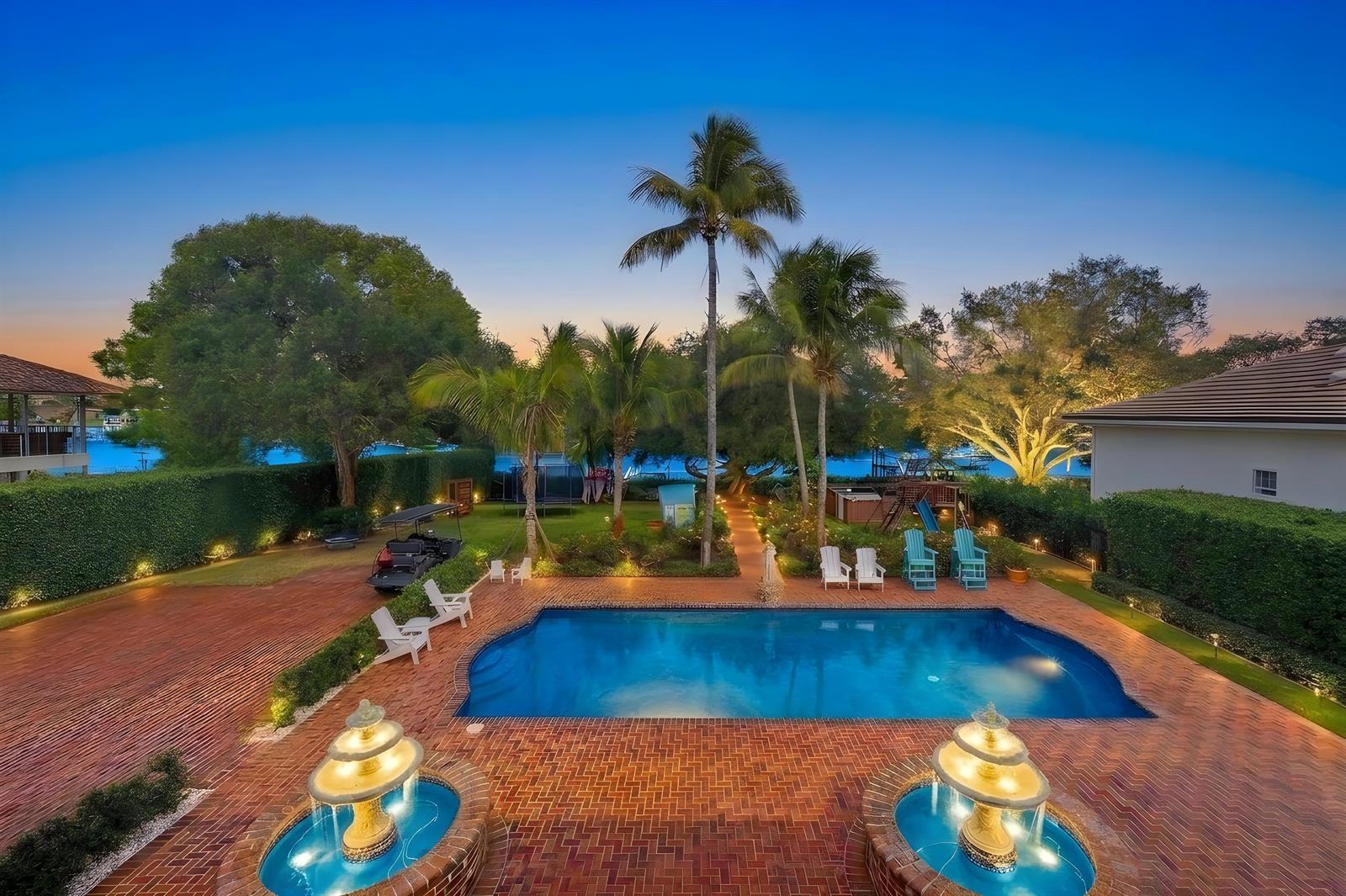 An outdoor swimming pool with two fountains sits on a brick patio near palm trees — 19153 SE Jupiter River Drive, Jupiter FL 33458, JUPITER, FL