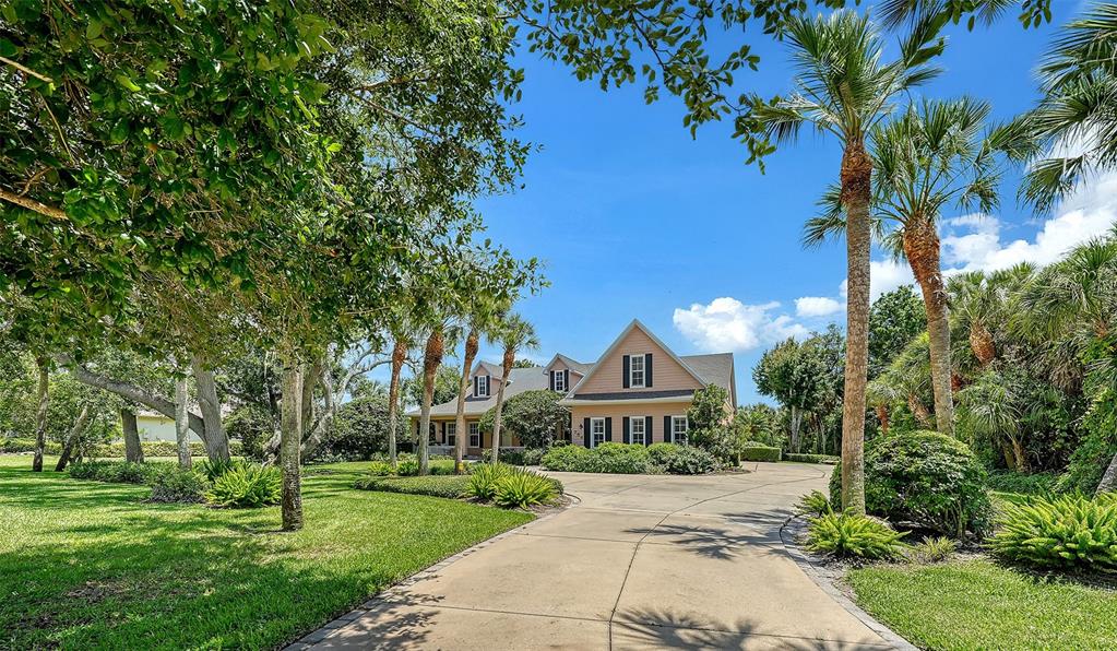 A two-story house with a beige exterior and a concrete driveway surrounded by palm trees — 756 VANDERBILT DRIVE, NOKOMIS, FL