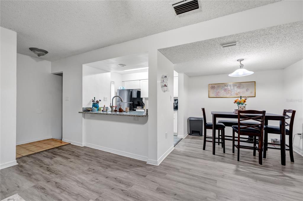 A dining area with wood-look flooring sits adjacent to a kitchen with a breakfast bar — 202 RIVERBEND DRIVE UNIT 103, ALTAMONTE SPRINGS, FL